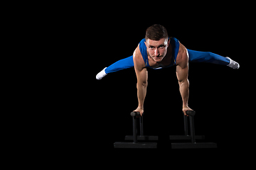 Image showing Muscular male gymnast training in gym, flexible and active. Caucasian fit guy, athlete in blue sportswear isolated on black