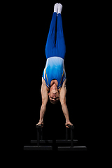 Image showing Muscular male gymnast training in gym, flexible and active. Caucasian fit guy, athlete in blue sportswear isolated on black