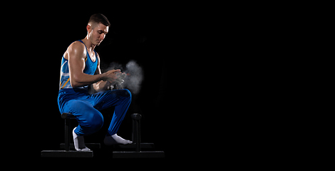 Image showing Muscular male gymnast training in gym, flexible and active. Caucasian fit guy, athlete in blue sportswear isolated on black