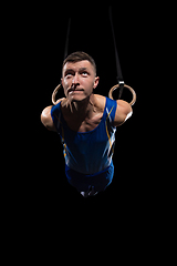 Image showing Muscular male gymnast training in gym, flexible and active. Caucasian fit guy, athlete in blue sportswear isolated on black