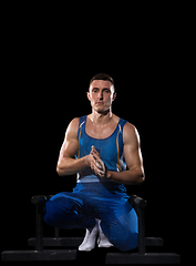 Image showing Muscular male gymnast training in gym, flexible and active. Caucasian fit guy, athlete in blue sportswear isolated on black