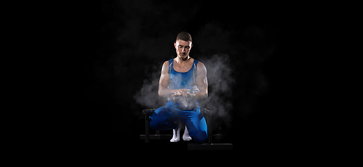 Image showing Muscular male gymnast training in gym, flexible and active. Caucasian fit guy, athlete in blue sportswear isolated on black