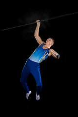 Image showing Muscular male gymnast training in gym, flexible and active. Caucasian fit guy, athlete in blue sportswear isolated on black