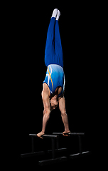 Image showing Muscular male gymnast training in gym, flexible and active. Caucasian fit guy, athlete in blue sportswear isolated on black