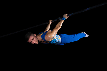 Image showing Muscular male gymnast training in gym, flexible and active. Caucasian fit guy, athlete in blue sportswear isolated on black