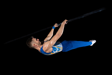 Image showing Muscular male gymnast training in gym, flexible and active. Caucasian fit guy, athlete in blue sportswear isolated on black