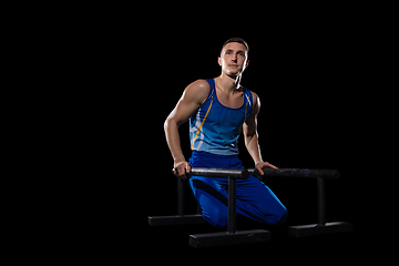 Image showing Muscular male gymnast training in gym, flexible and active. Caucasian fit guy, athlete in blue sportswear isolated on black