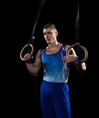 Image showing Muscular male gymnast training in gym, flexible and active. Caucasian fit guy, athlete in blue sportswear isolated on black