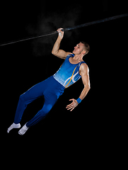 Image showing Muscular male gymnast training in gym, flexible and active. Caucasian fit guy, athlete in blue sportswear isolated on black