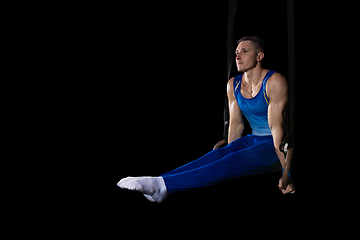 Image showing Muscular male gymnast training in gym, flexible and active. Caucasian fit guy, athlete in blue sportswear isolated on black