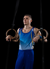 Image showing Muscular male gymnast training in gym, flexible and active. Caucasian fit guy, athlete in blue sportswear isolated on black