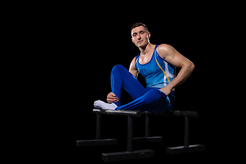 Image showing Muscular male gymnast training in gym, flexible and active. Caucasian fit guy, athlete in blue sportswear isolated on black