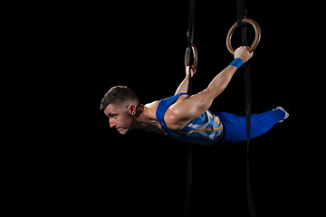 Image showing Muscular male gymnast training in gym, flexible and active. Caucasian fit guy, athlete in blue sportswear isolated on black