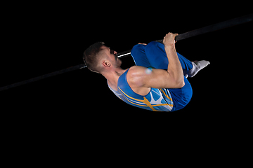 Image showing Muscular male gymnast training in gym, flexible and active. Caucasian fit guy, athlete in blue sportswear isolated on black