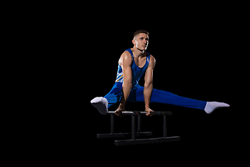 Image showing Muscular male gymnast training in gym, flexible and active. Caucasian fit guy, athlete in blue sportswear isolated on black