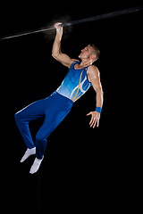 Image showing Muscular male gymnast training in gym, flexible and active. Caucasian fit guy, athlete in blue sportswear isolated on black