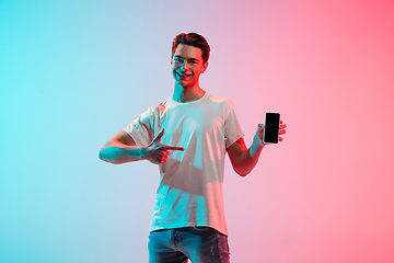 Image showing Young caucasian man\'s portrait on gradient blue-pink studio background in neon light