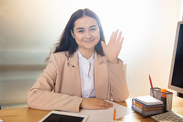 Image showing Young woman talking, working during videoconference with colleagues at home office