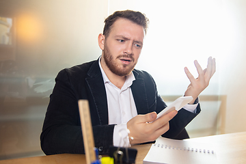 Image showing Young man talking, working during videoconference with colleagues at home office