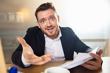 Image showing Young man talking, working during videoconference with colleagues at home office