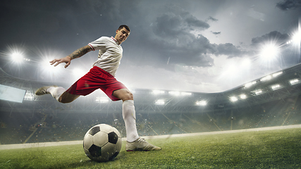 Image showing Young man football player kicking ball while match at stadium. Flyer for ad, design.