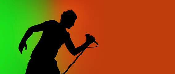 Image showing Silhouette of young caucasian male singer isolated on green-orange gradient studio background in neon light