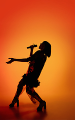 Image showing Silhouette of young caucasian female singer isolated on orange gradient studio background in neon light