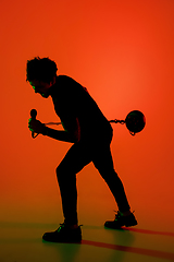 Image showing Silhouette of young caucasian male singer isolated on orange gradient studio background in neon light