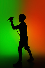 Image showing Silhouette of young caucasian male singer isolated on green-orange gradient studio background in neon light