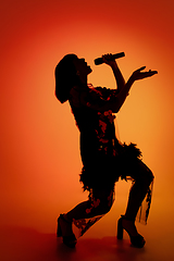 Image showing Silhouette of young caucasian female singer isolated on orange gradient studio background in neon light