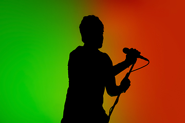 Image showing Silhouette of young caucasian male singer isolated on green-orange gradient studio background in neon light