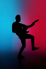 Image showing Silhouette of young caucasian male guitarist isolated on blue-pink gradient studio background in neon light