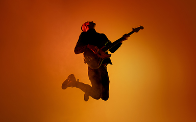 Image showing Silhouette of young caucasian male guitarist isolated on orange gradient studio background in neon light