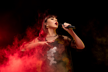 Image showing Caucasian female singer portrait isolated on dark studio background in neon light