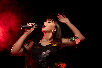 Image showing Caucasian female singer portrait isolated on dark studio background in neon light