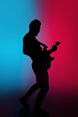 Image showing Silhouette of young caucasian male guitarist isolated on blue-pink gradient studio background in neon light