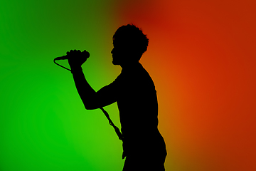 Image showing Silhouette of young caucasian male singer isolated on green-orange gradient studio background in neon light