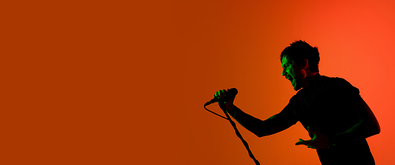 Image showing Silhouette of young caucasian male singer isolated on orange gradient studio background in neon light
