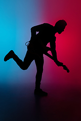 Image showing Silhouette of young caucasian male guitarist isolated on blue-pink gradient studio background in neon light