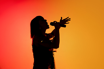 Image showing Silhouette of young caucasian female singer isolated on orange gradient studio background in neon light