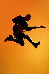 Image showing Silhouette of young caucasian male guitarist isolated on orange gradient studio background in neon light