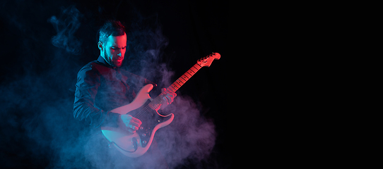 Image showing Silhouette of young caucasian male guitarist isolated on blue-pink gradient studio background in neon light