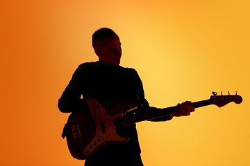 Image showing Silhouette of young caucasian male guitarist isolated on orange gradient studio background in neon light