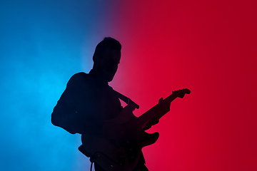 Image showing Silhouette of young caucasian male guitarist isolated on blue-pink gradient studio background in neon light