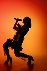 Image showing Silhouette of young caucasian female singer isolated on orange gradient studio background in neon light