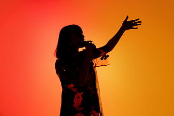 Image showing Silhouette of young caucasian female singer isolated on orange gradient studio background in neon light