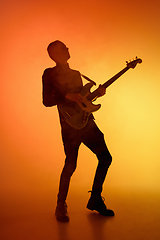 Image showing Silhouette of young caucasian male guitarist isolated on orange gradient studio background in neon light