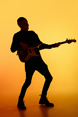 Image showing Silhouette of young caucasian male guitarist isolated on orange gradient studio background in neon light