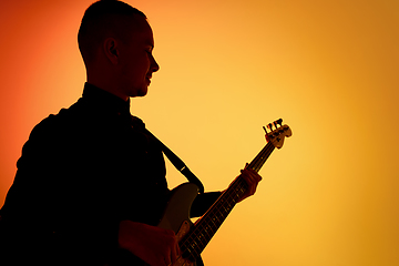 Image showing Silhouette of young caucasian male guitarist isolated on orange gradient studio background in neon light