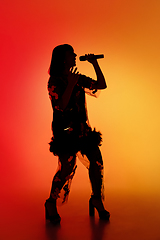 Image showing Silhouette of young caucasian female singer isolated on orange gradient studio background in neon light